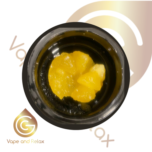 A close-up of a glass container holding yellow, waxy CBD Gold 90% Cannabinoids | 1:1 CBD/THCA extract rests on a background with the gold and brown Vape and Relax logo and text.